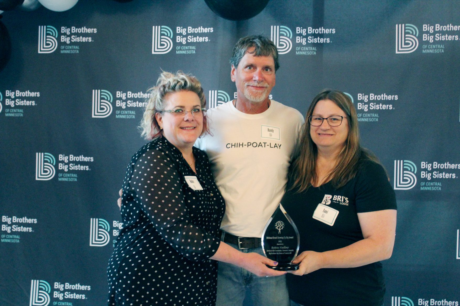 Three adults - Robin Hadley and Randy and Tami Kruzel - pose with an award in front of a Big Brothers Big Sisters backdrop